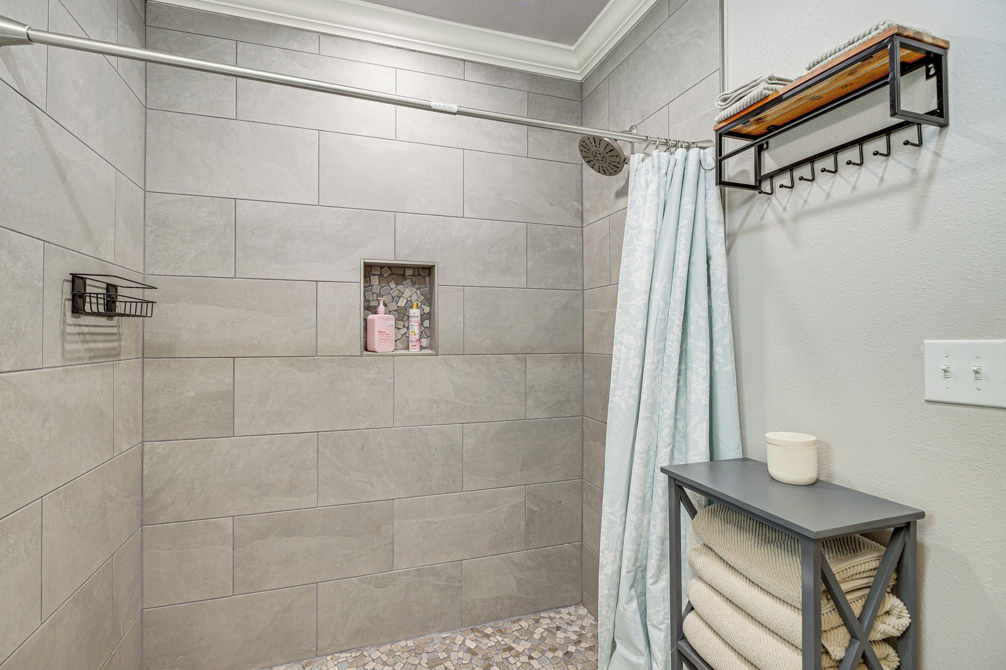 A shower area with tiled walls, a shower curtain, a towel rack, and a small shelf with toiletries.