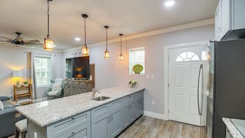 A kitchen with granite countertops, grey cabinets, a stainless steel refrigerator, pendant lights, and a ceiling fan.
