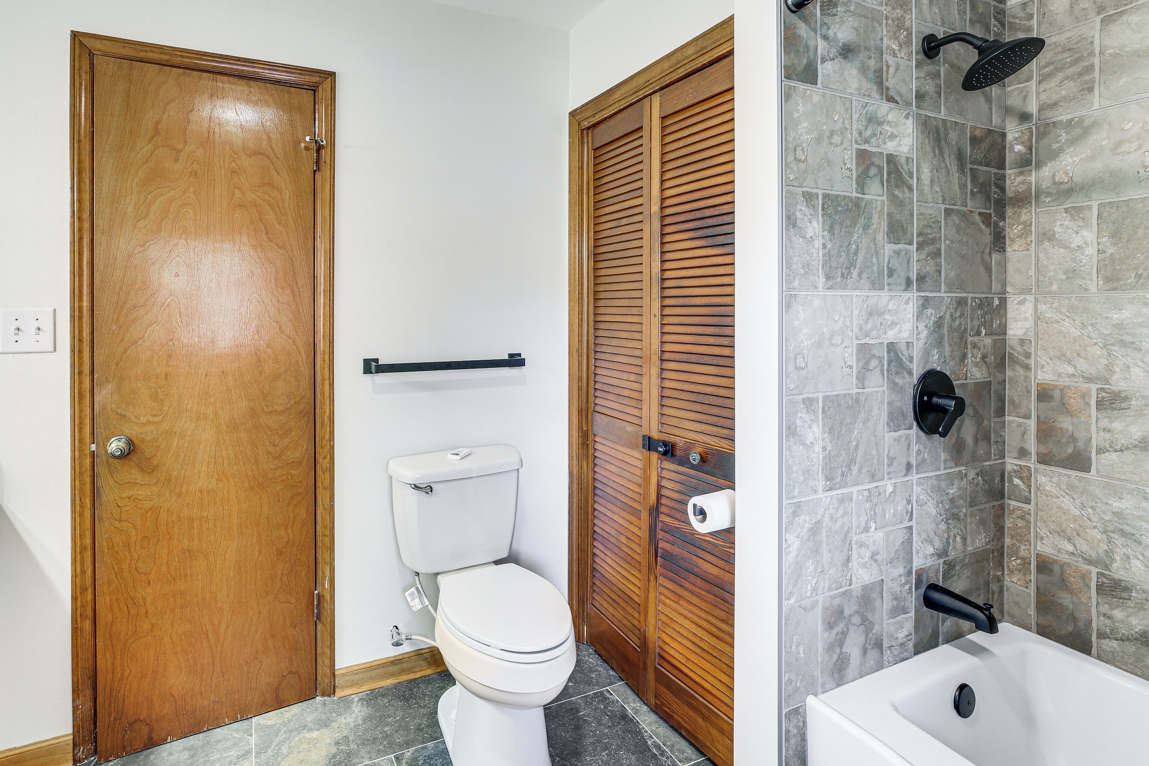 Un baño con puerta de madera, inodoro, ducha con grifo negro y pared de azulejos.