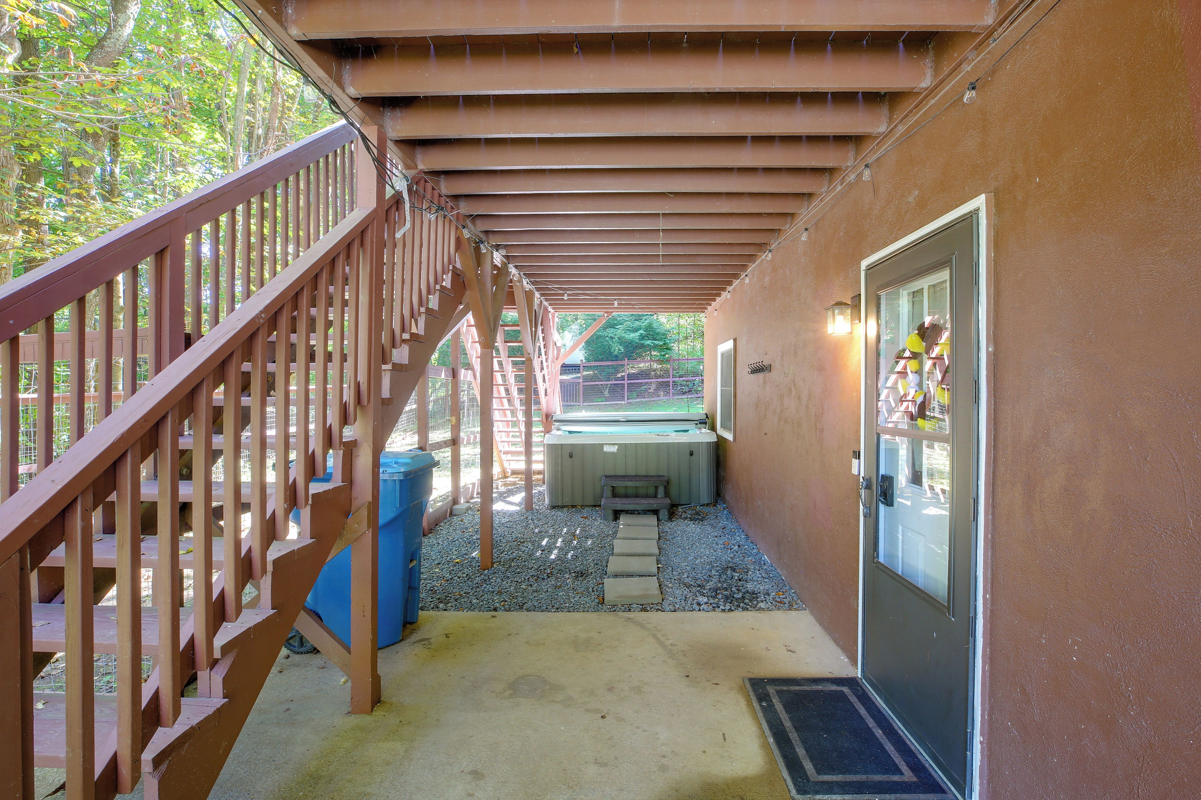 A covered outdoor area with a wooden staircase, a hot tub, and a door with a window.