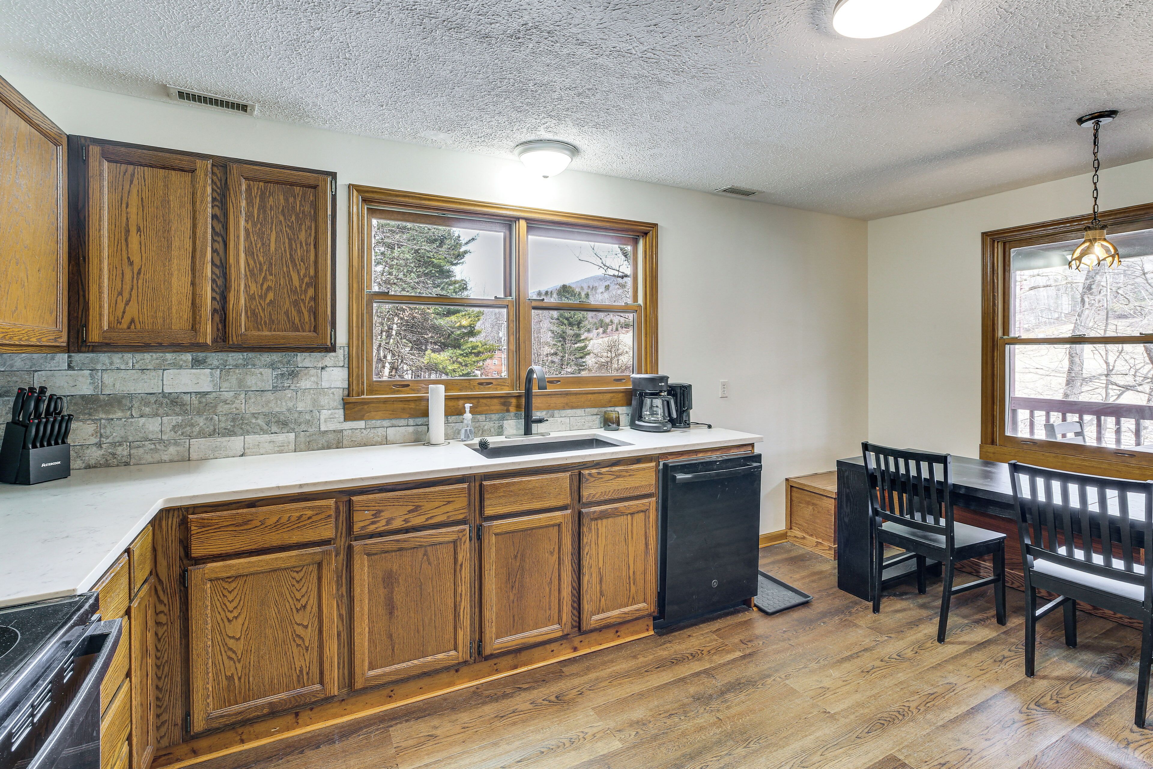 A kitchen with wooden cabinets, a dishwasher, a sink, and a dining area with chairs and a table.