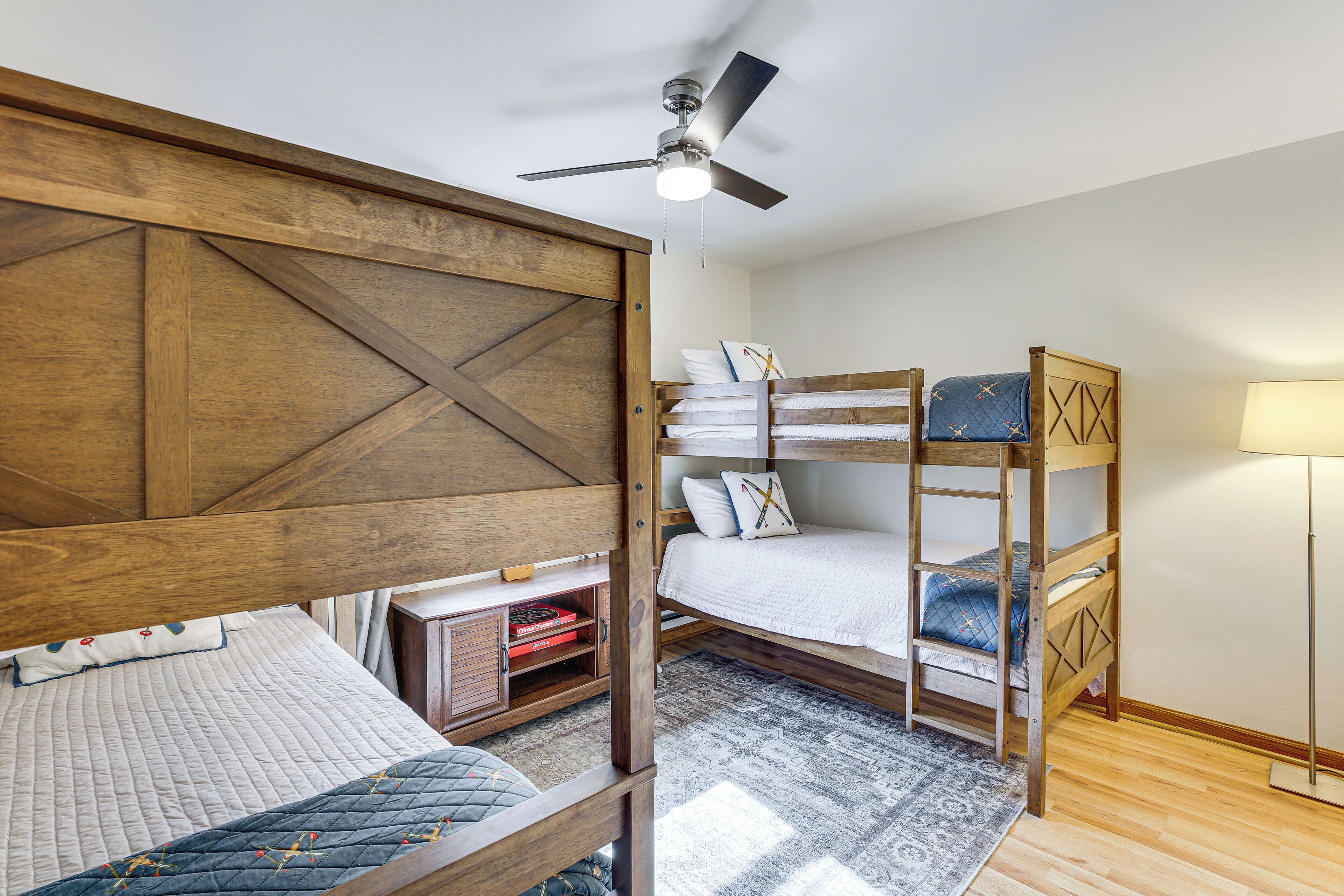 A bedroom with two bunk beds, a ceiling fan, a bedside table with a lamp, and a patterned rug.