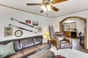 A living room with a brown leather sofa, a brown leather armchair, a ceiling fan, and skis mounted on the wall. - Raley's Retreat w/ Hot Tub: 2 Mi to Dtwn Boone! (Boone)