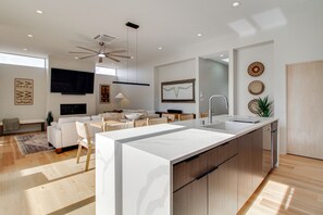A modern kitchen with a central island, a dining area with a sofa and chairs, and a ceiling fan. - Sunnyside View: ABQ Home Near Old Town & Biopark! (Albuquerque)