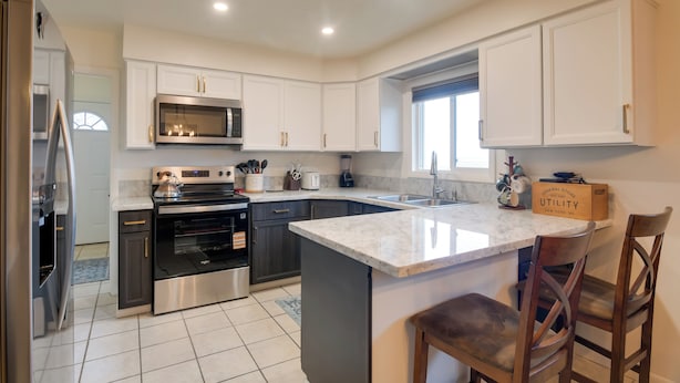 A modern kitchen with white cabinets, stainless steel appliances, and a large island with bar stools. - 5 Mi to Heise Hot Springs: 'the Trout House' (Ririe)