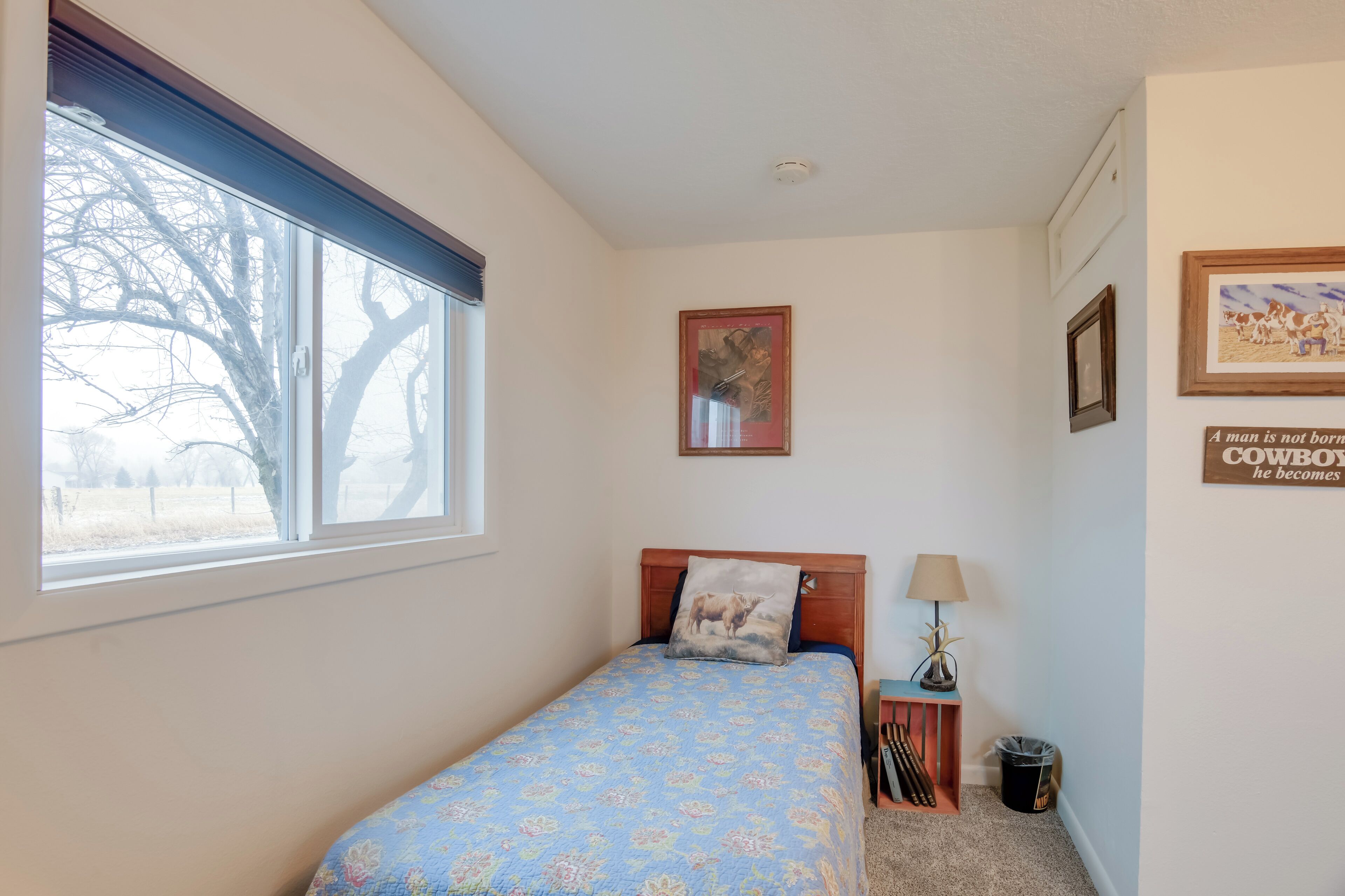 Ein Schlafzimmer mit einem Bett, einem Fenster, einem Nachttisch und einer Wand mit gerahmten Bildern.