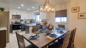 A modern kitchen with white cabinets, stainless steel appliances, and a dining area set for six with blue plates and a chandelier. - 5 Mi to Heise Hot Springs: 'the Trout House' (Ririe)