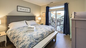A bedroom with a bed, a nightstand, a ceiling fan, a window with curtains, and a view of the outside. - Bay-n-beach! Comfy Coastal Condo in Lewes! (Lewes)