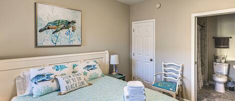 A bedroom with a bed, a nightstand, a chair, a door, and a bathroom visible through an open door.