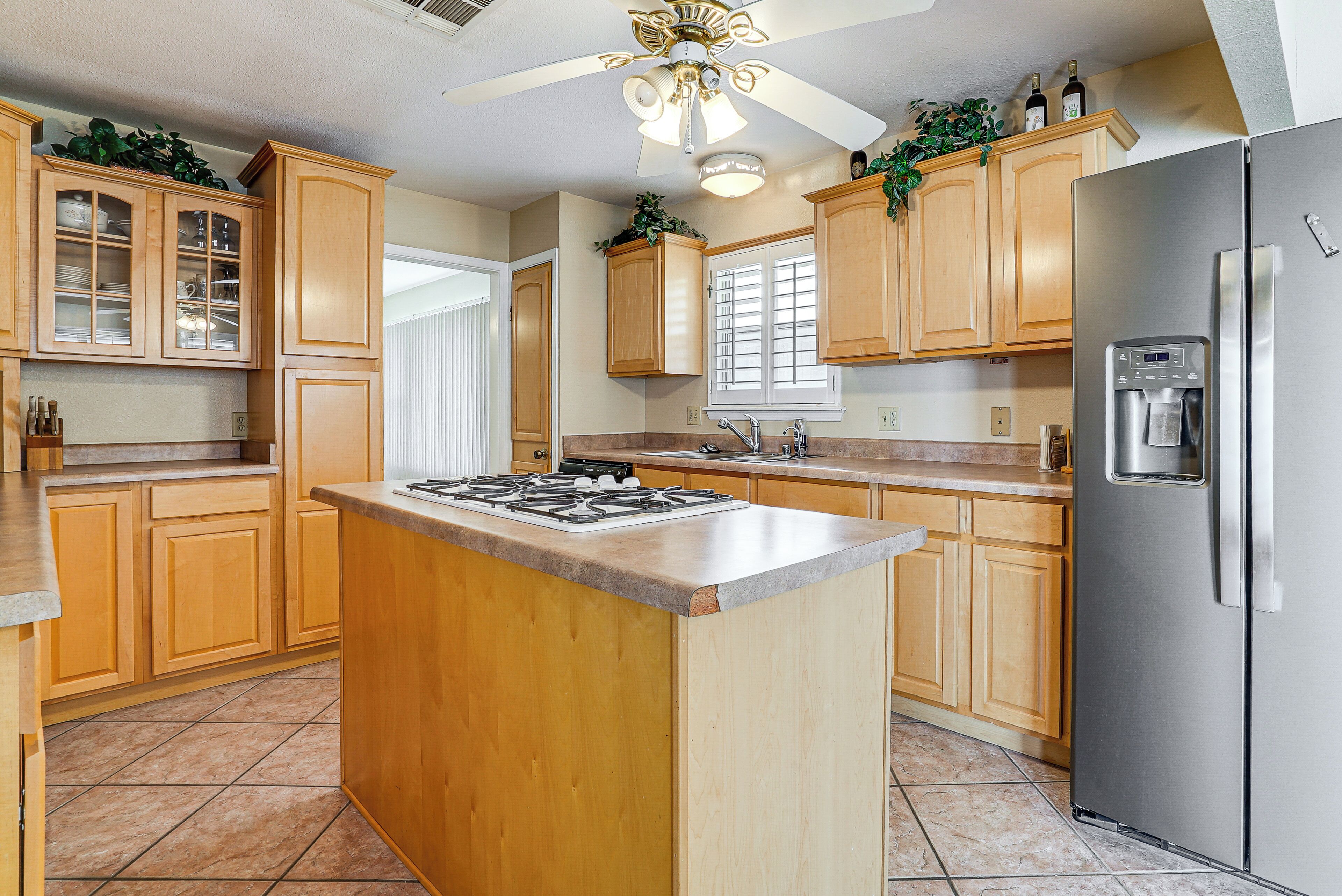 A kitchen with wooden cabinets, a stainless steel refrigerator, a gas stove, and a ceiling fan.