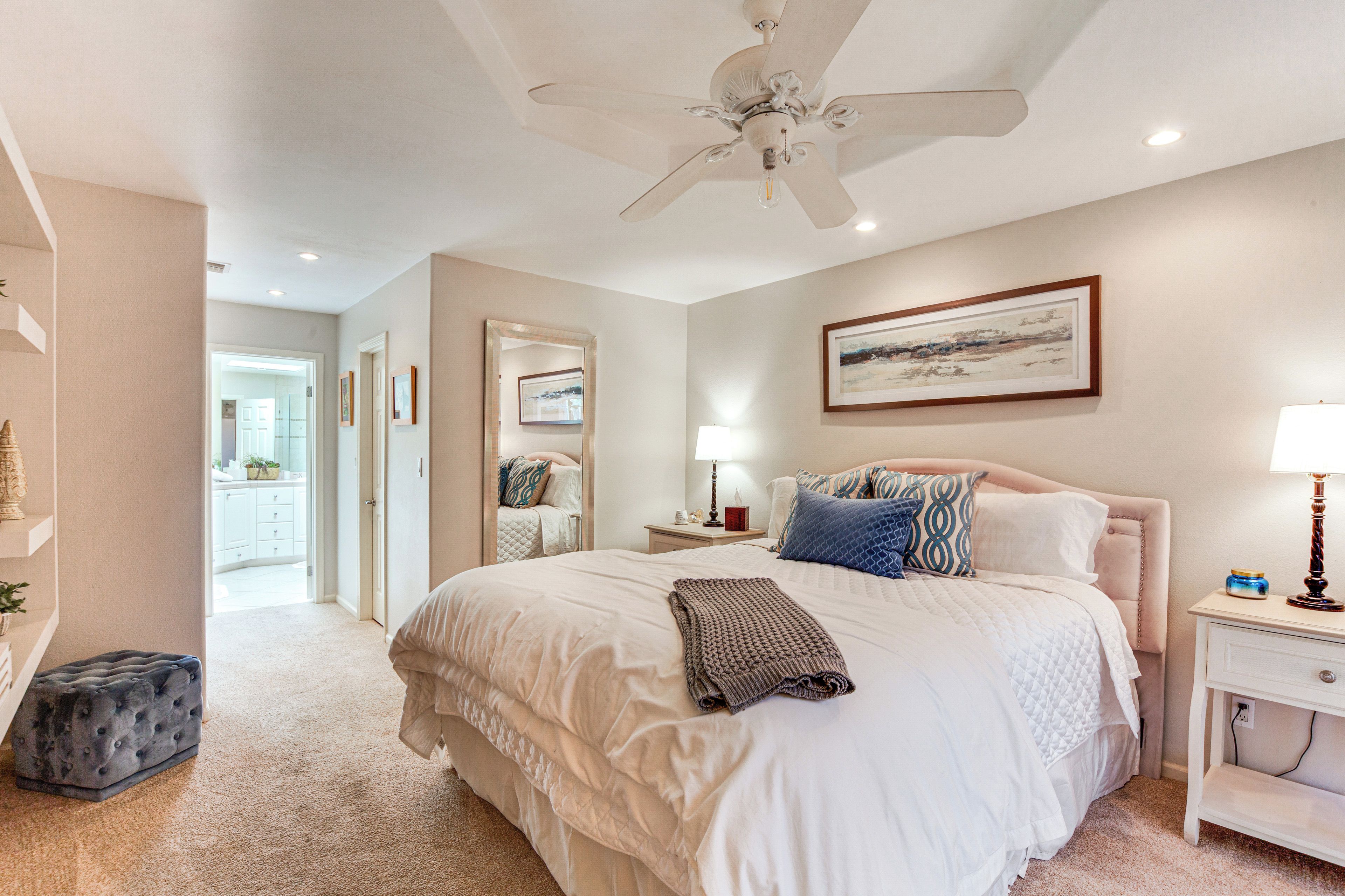 A bedroom with a large bed, a ceiling fan, a bedside table with a lamp, and a framed picture on the wall.