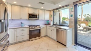 A modern kitchen with white cabinets, stainless steel appliances, and a large window overlooking a patio area. - 11 Mi to Coachella: Palm Desert Gem w/ Pool Access (Palm Desert)