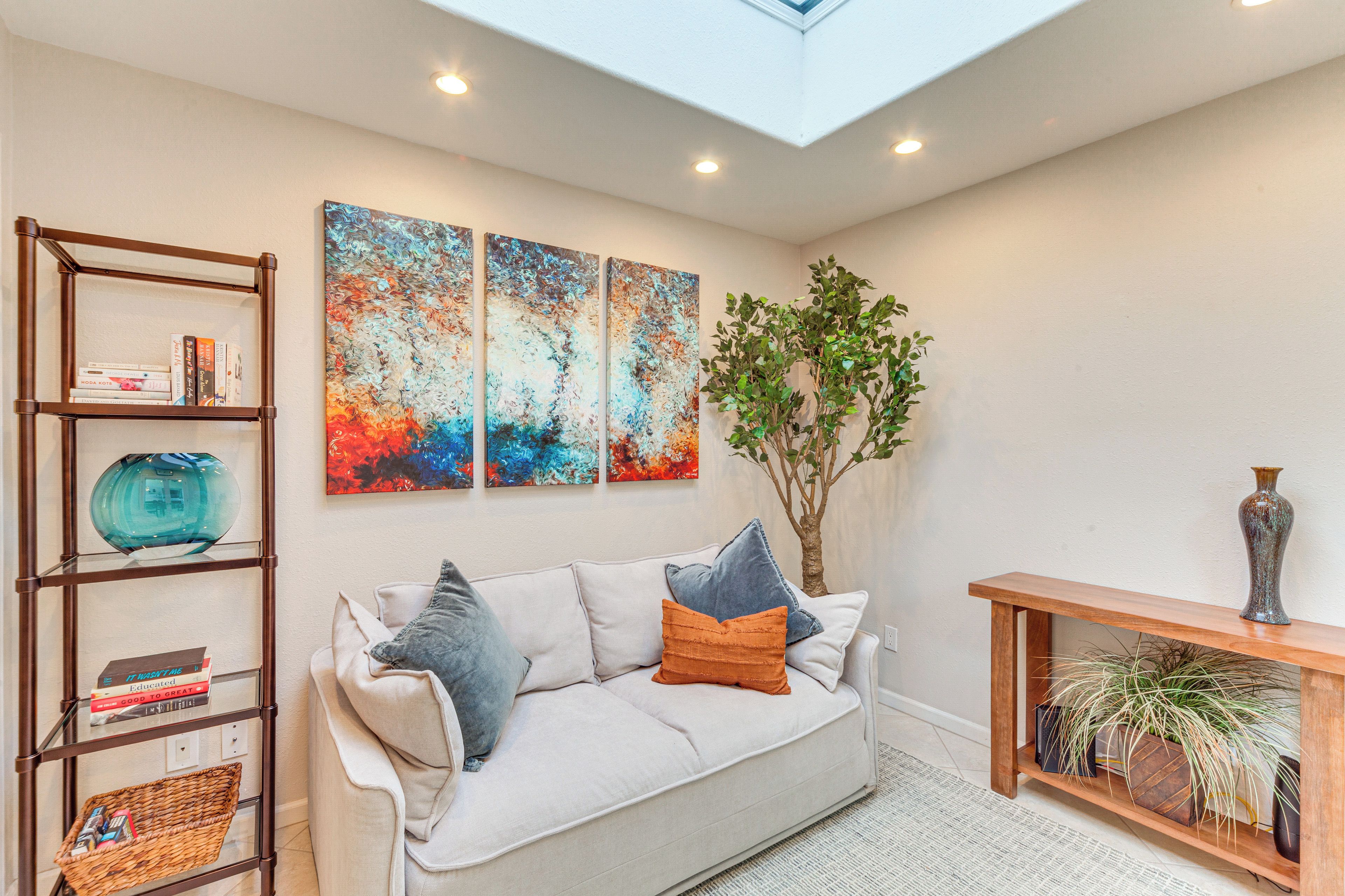 A living room with a sofa, a wooden console table, a bookshelf, and abstract wall art.