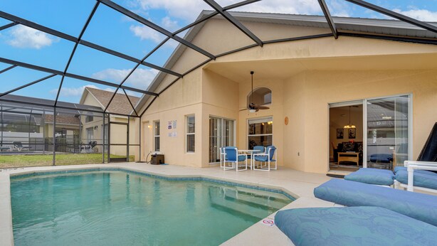 A pool area with a glass enclosure, a ceiling fan, and blue lounge chairs. - Poolside Oasis & Game Room Fun! Gem in Haines City (Haines City)