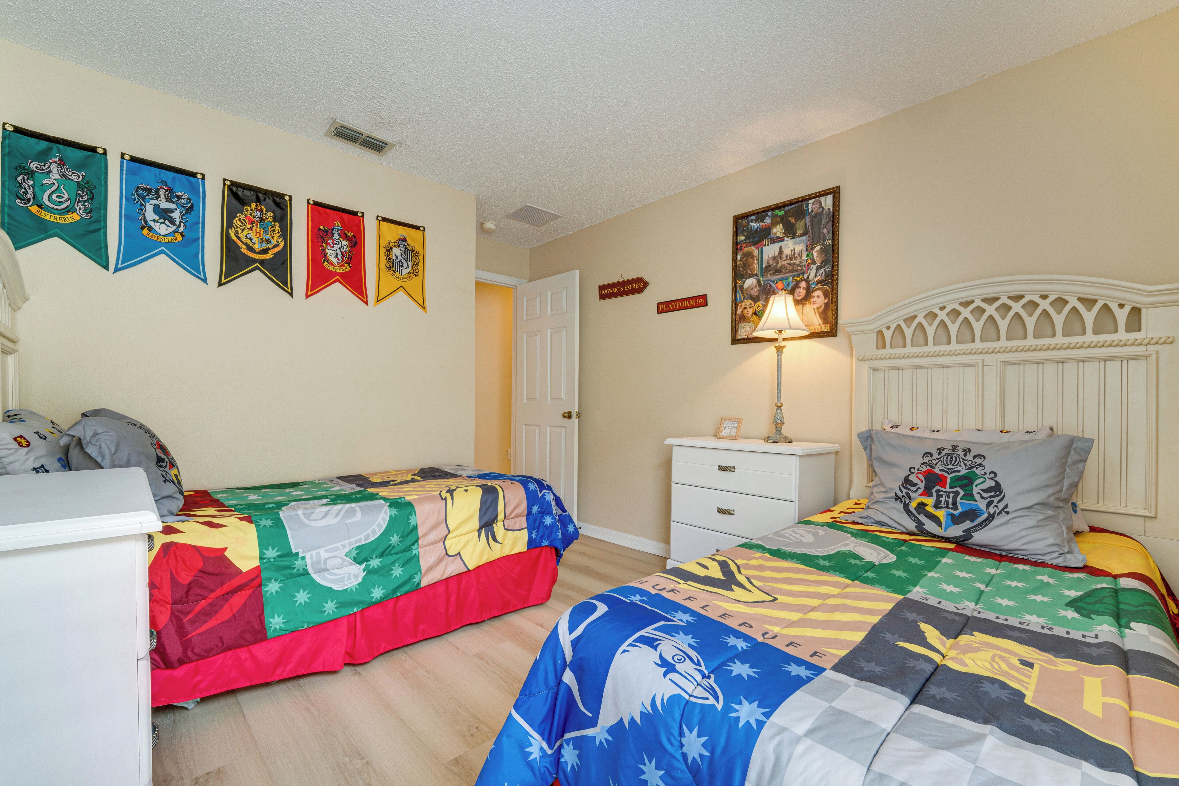 A bedroom with two beds, a white dresser, a nightstand, and a wall with flags.