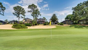 A golf course with a flagstick, sand bunkers, and residential buildings in the background. - Poolside Oasis & Game Room Fun! Gem in Haines City (Haines City)