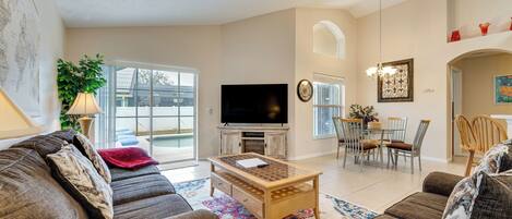 A spacious living room with a large TV, comfortable sofas, a wooden coffee table, and a dining area with chairs and a table.