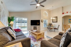 A spacious living room with a large TV, comfortable sofas, a wooden coffee table, and a dining area with chairs and a table. - Poolside Oasis & Game Room Fun! Gem in Haines City (Haines City)