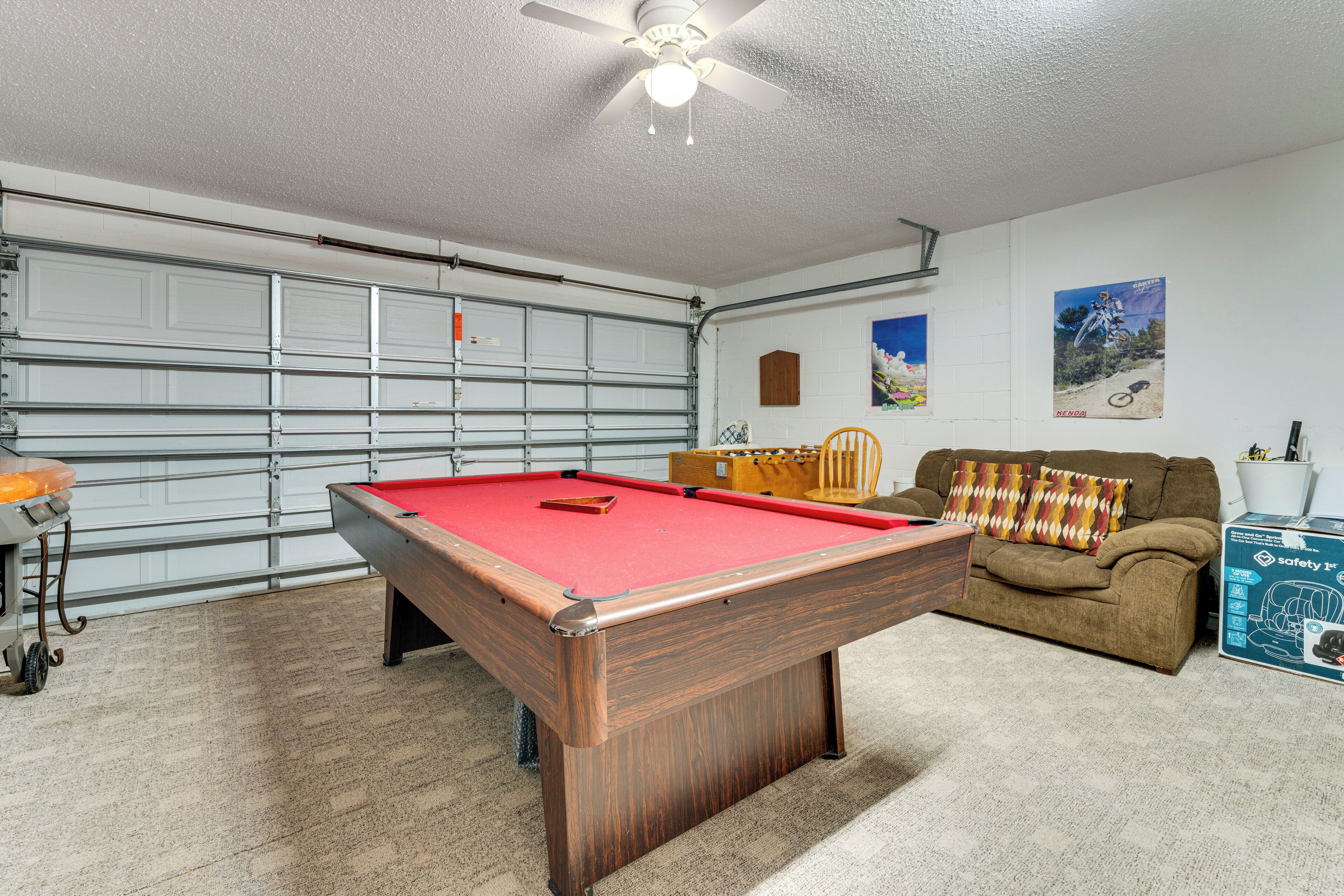 Une table de billard dans une pièce qui comprend une porte de garage, un canapé et une affiche accrochée au mur.