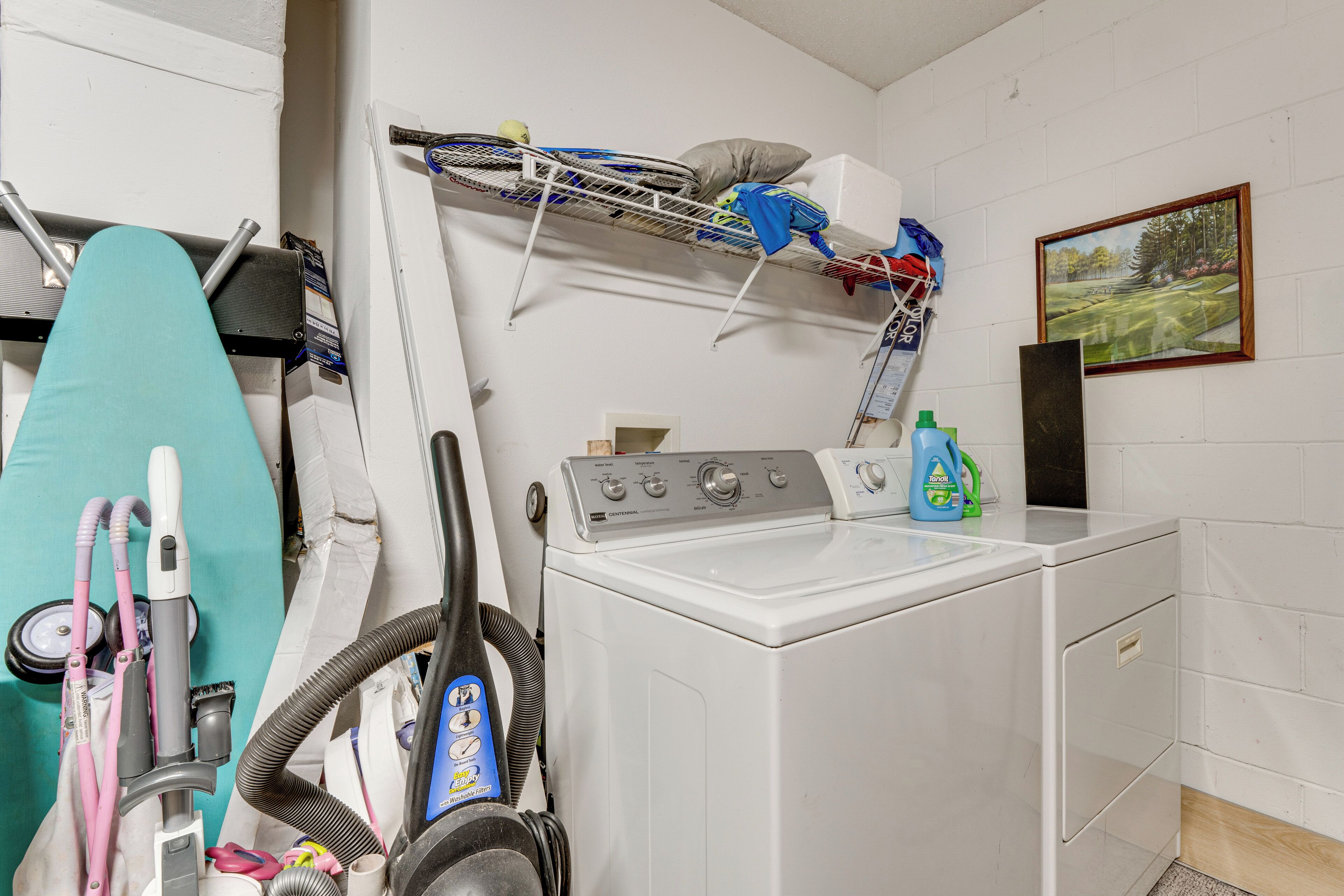 A laundry room with a washing machine, ironing board, and various cleaning supplies.