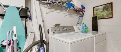 A laundry room with a washing machine, ironing board, and various cleaning supplies.