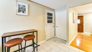 Ein Flur mit einer weißen Tür, einem gerahmten Bild an der Wand und einem Holztisch mit zwei Hocker.