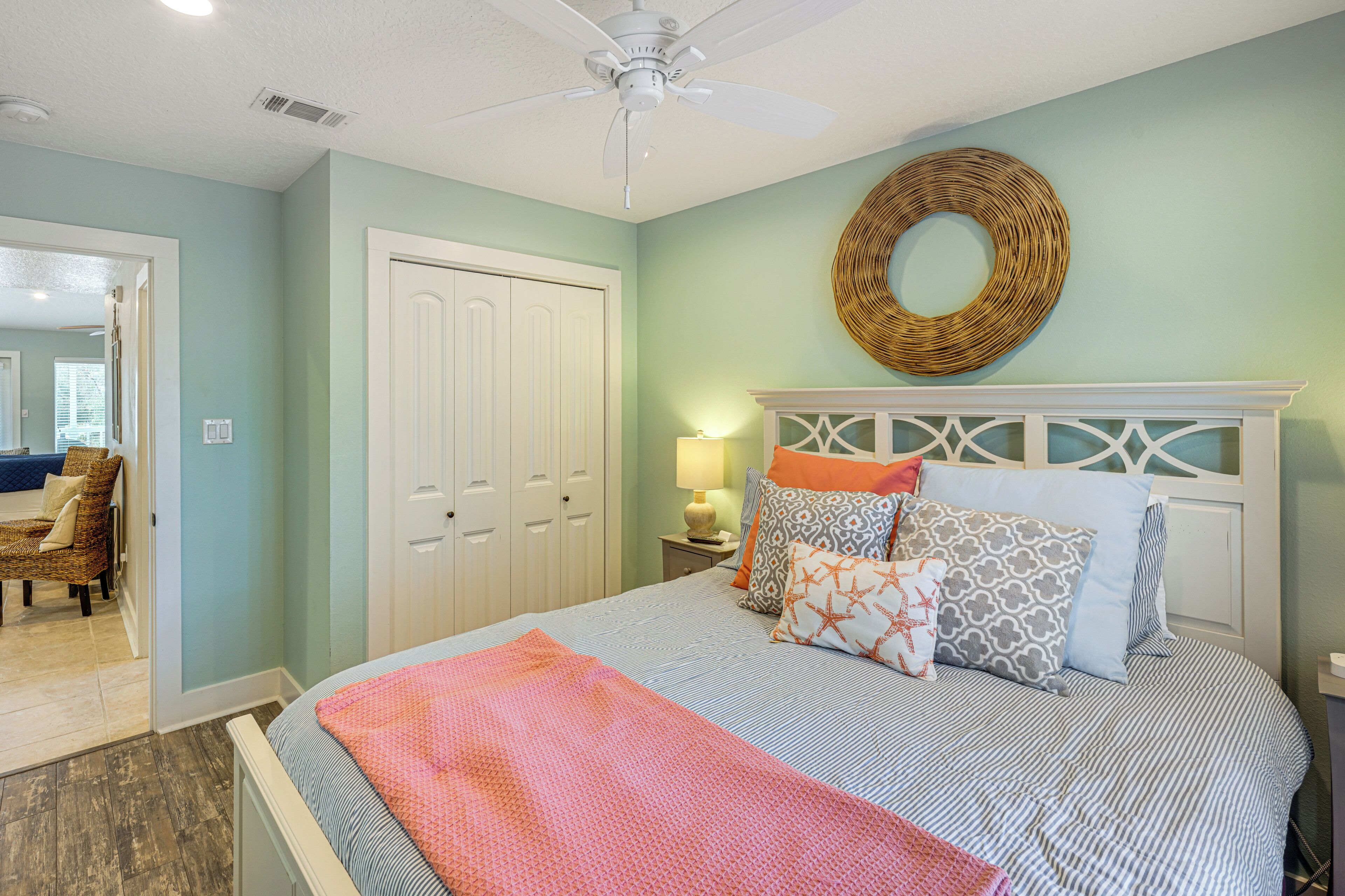 Une chambre à coucher avec un lit, un ventilateur de plafond, une décoration murale en osier et une porte.