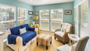 A cozy room with a blue quilted sofa, a wicker chair, and a patterned ottoman.