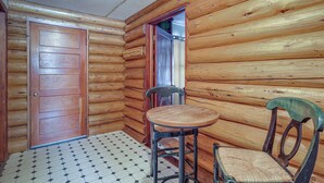 Interior de una cabaña de troncos con una puerta de madera, una pequeña mesa redonda y una silla.