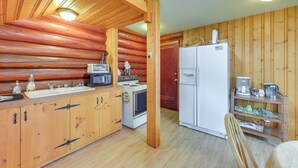 Une cuisine aménagée dans le style d’un chalet en rondins, avec des murs en bois, un plafond en bois, un évier, une cuisinière, un réfrigérateur et une chaise en bois.