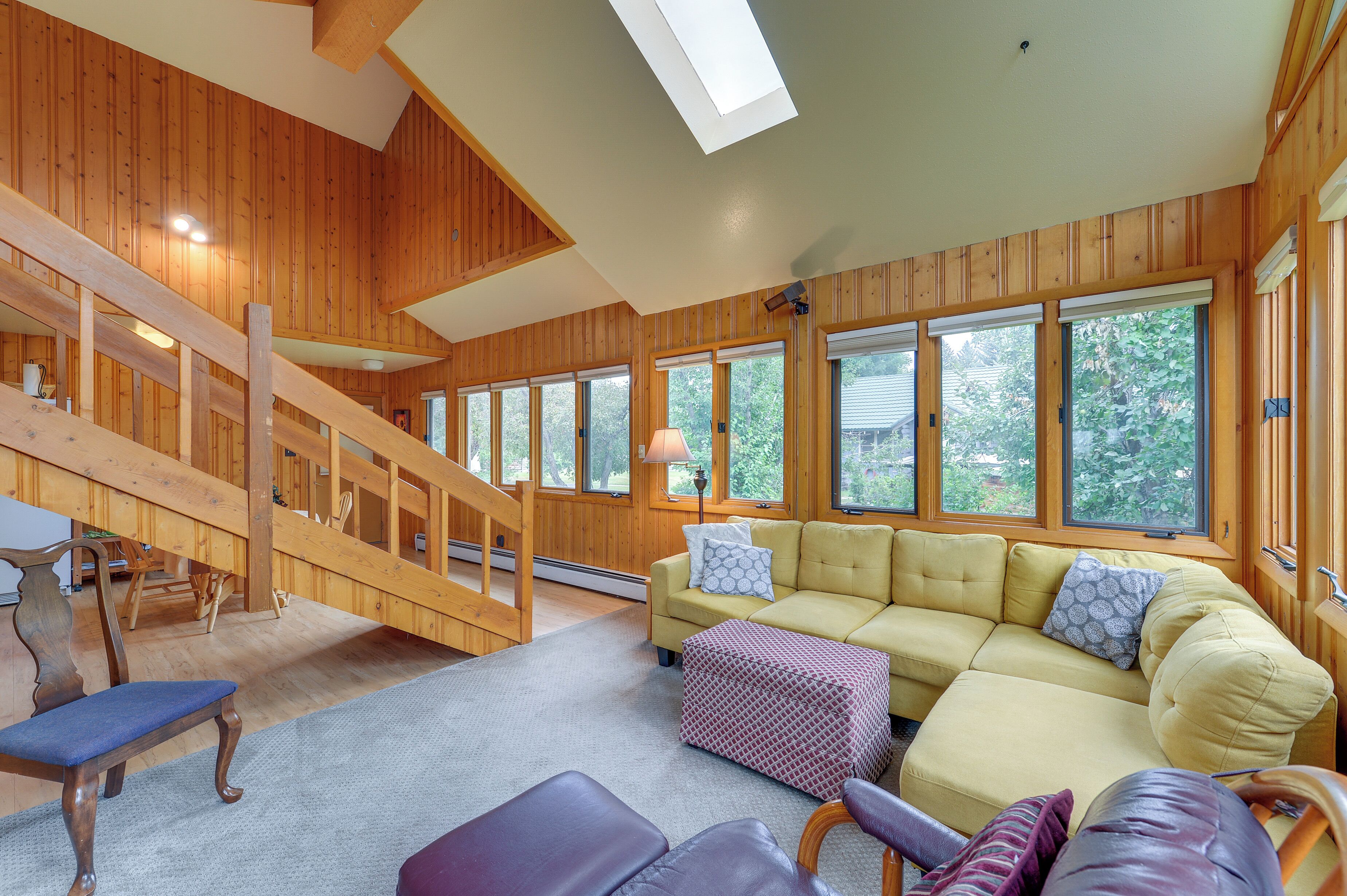 A wooden interior with a staircase, a yellow sofa, and a large window.