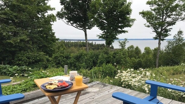 A wooden deck with a table set for breakfast, overlooking a lake. - Private Beach! Passamaquoddy Bay Cottage (Perry)