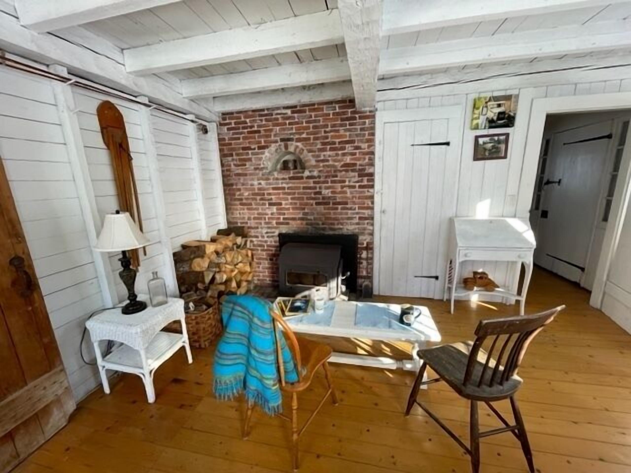 A cozy room with a brick fireplace, wooden flooring, and white furniture.