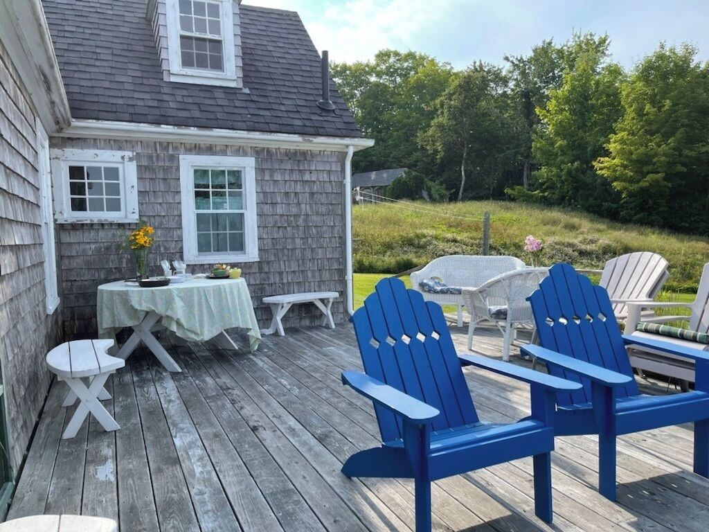 Una terraza de madera con sillas Adirondack, una mesita y una silla blanca.
