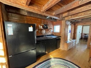 A rustic kitchen with wooden beams, a black refrigerator, and a sink. - Private Beach! Passamaquoddy Bay Cottage (Perry)