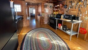 A rustic kitchen with exposed wooden beams, a black refrigerator, a microwave, and a pegboard with kitchen utensils. - Private Beach! Passamaquoddy Bay Cottage (Perry)