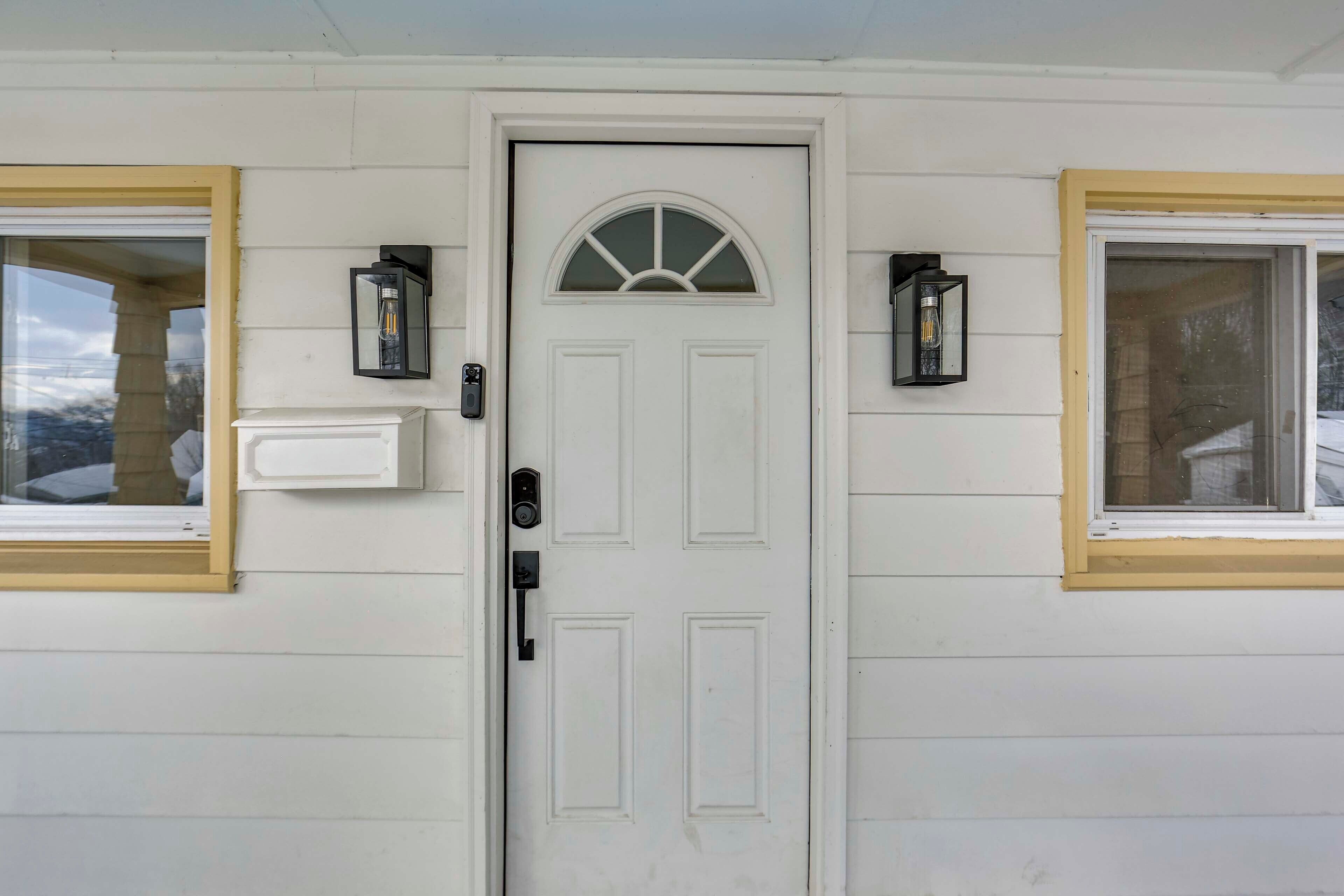 A white front door with a semi-circular window above it, flanked by two wall-mounted lantern-style lights.