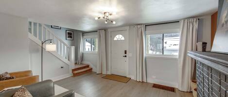 A spacious living room with a staircase, a fireplace, and a large window with curtains.