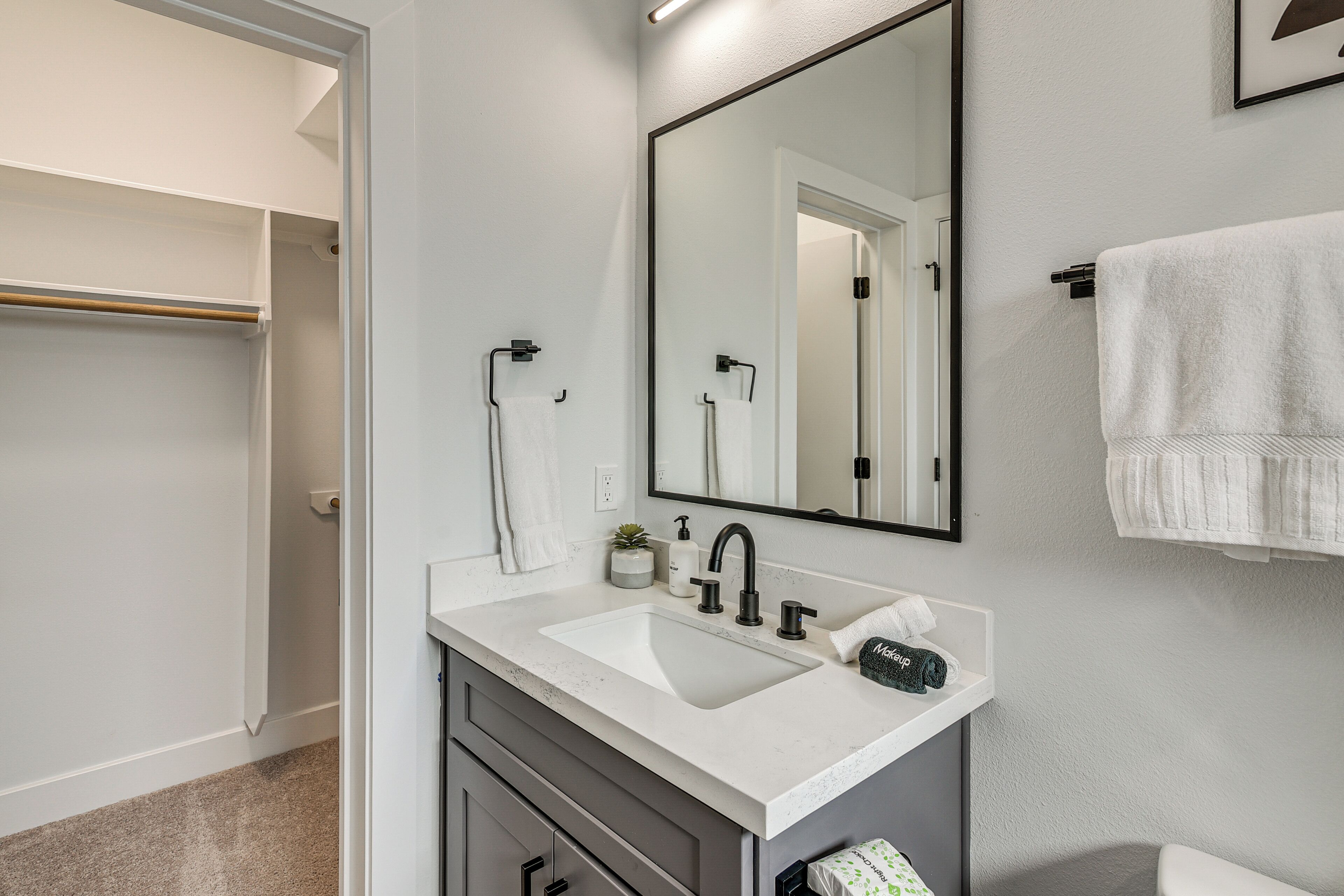 Un baño moderno con un lavamanos blanco, grifo negro y un espejo grande.
