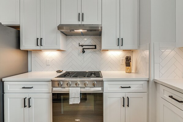 A modern kitchen with white cabinetry, a stainless steel range hood, and a herringbone-patterned backsplash. - Sleek & Spacious! Prime Houston Home Near NRG (Houston)