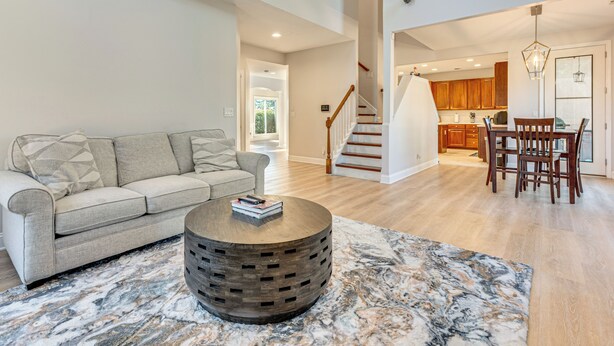 A spacious living area with a sofa, a round coffee table, and a marble rug. A staircase leads to a kitchen with wooden cabinets and a dining area with a table and chairs. - Outdoor Kitchen! Spacious Stone Mountain Retreat (Stone Mountain)