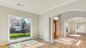 A spacious hallway with hardwood flooring, a colorful play mat, and a large window offering a view of a brick house. - Outdoor Kitchen! Spacious Stone Mountain Retreat (Stone Mountain)