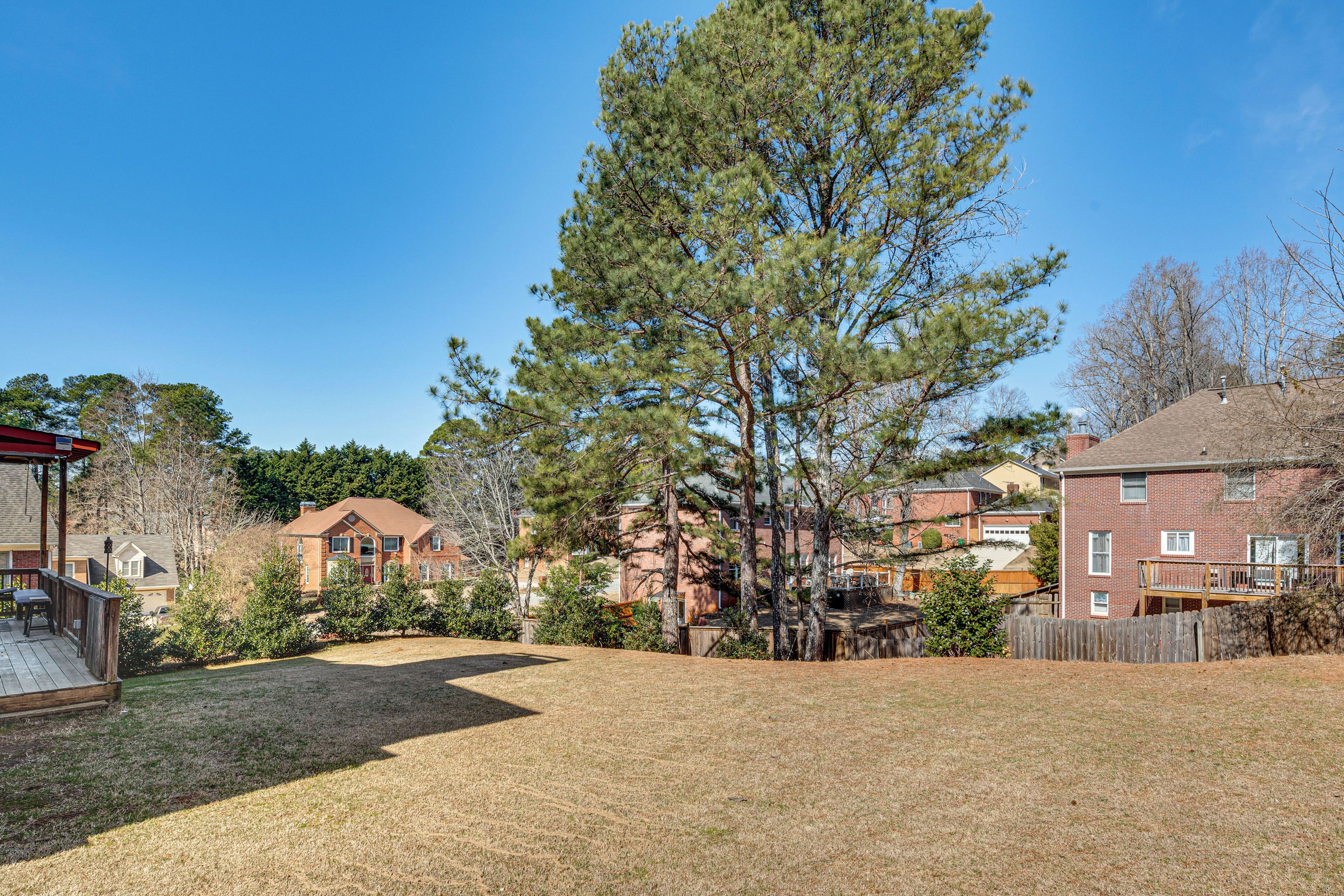 A residential backyard with a wooden deck, a large pine tree, and a brick house in the background.