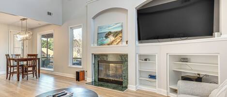 A spacious living room with a fireplace, a large TV, and a dining area with chairs and a table.
