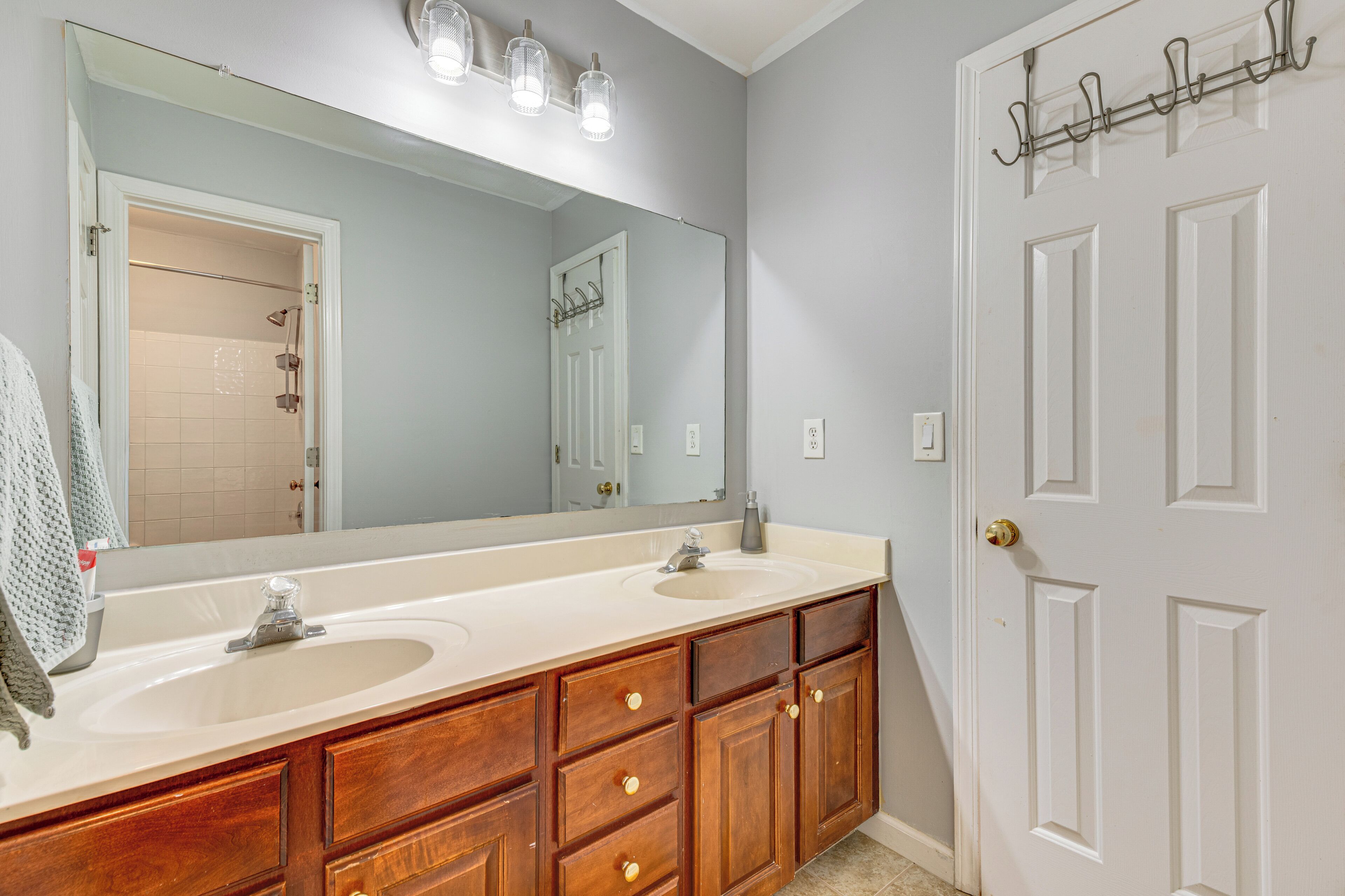 A bathroom with a double sink vanity, a large mirror, and a white door with a coat rack.
