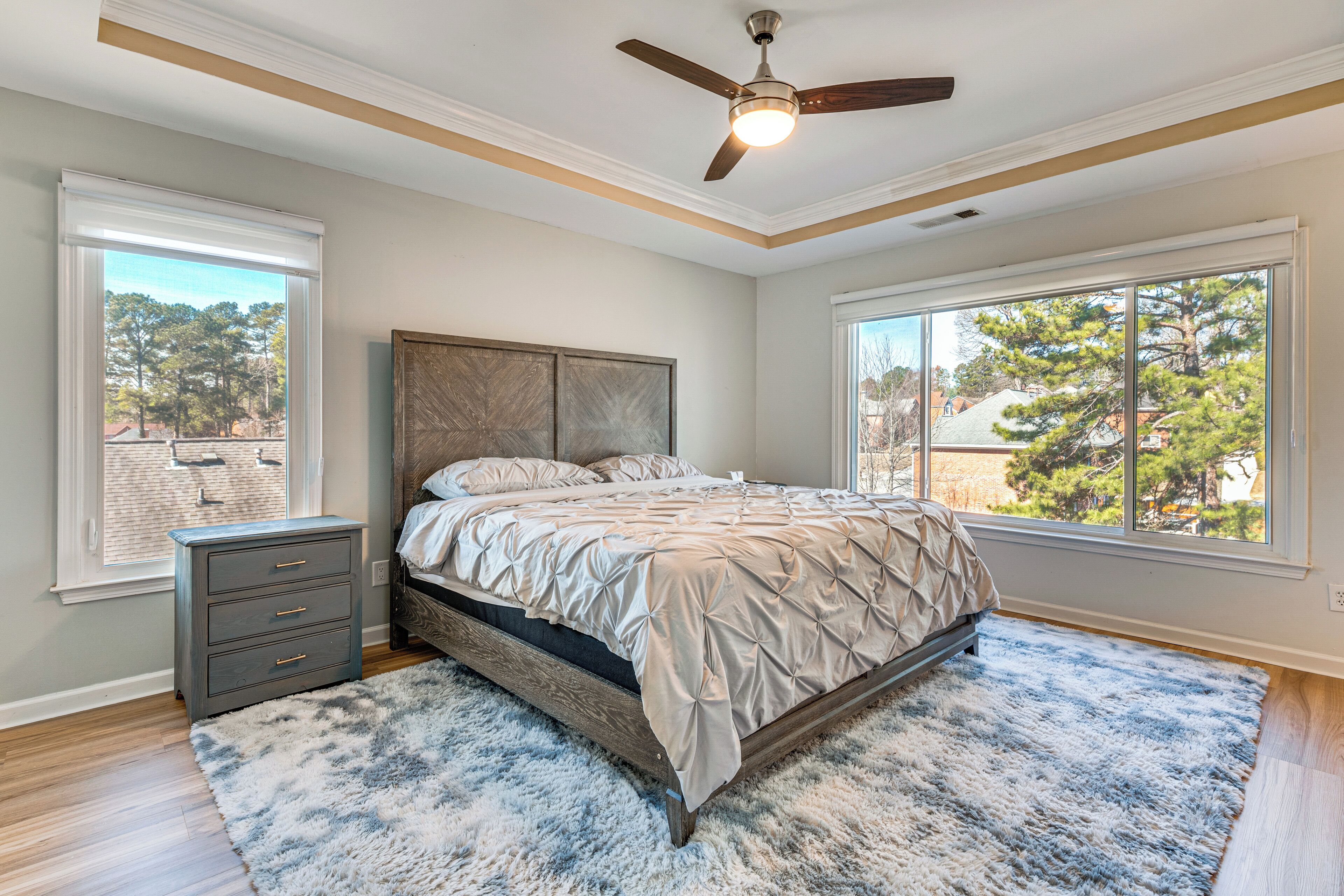 A bedroom with a bed, a nightstand, a ceiling fan, and large windows.