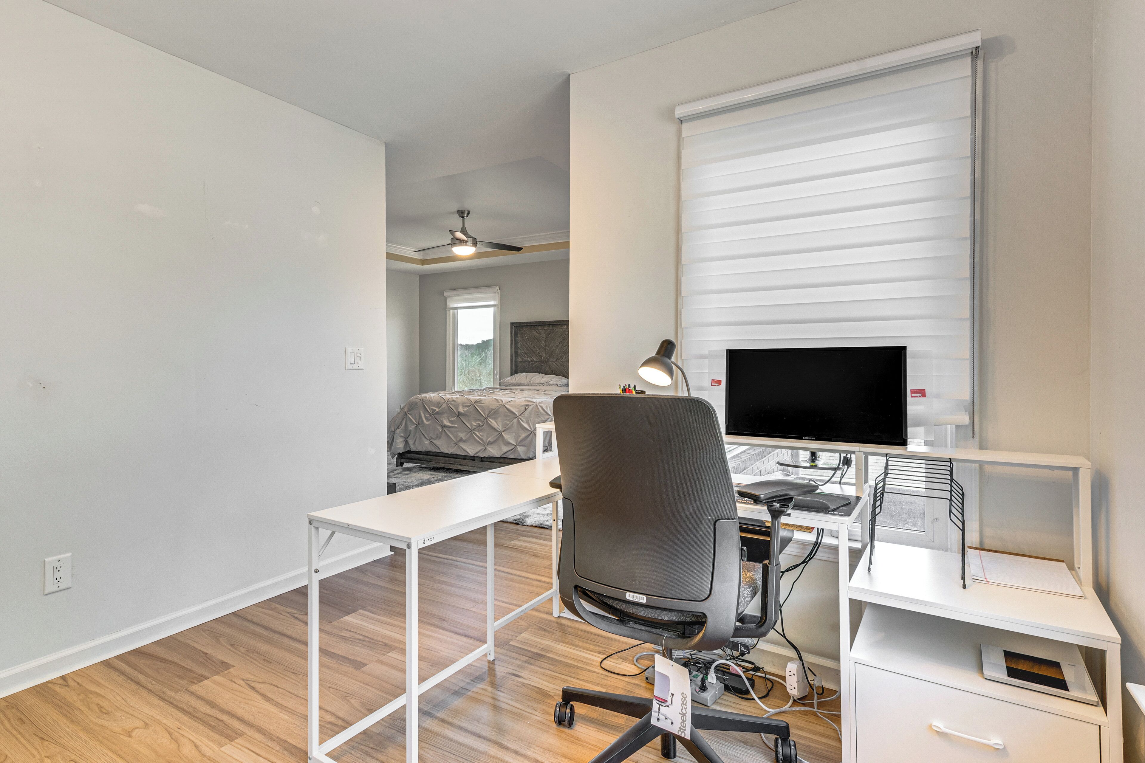 A modern bedroom with a bed, a desk with a computer, and a ceiling fan.