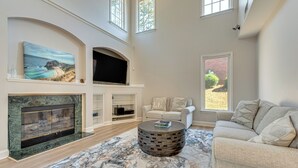 A spacious living room with a fireplace, a large painting, a comfortable sofa, and a round coffee table. - Outdoor Kitchen! Spacious Stone Mountain Retreat (Stone Mountain)