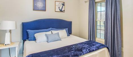 Una cama bien hecha con dosel azul, una mesita de noche con lámpara y dos cuadros en la pared.