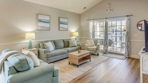 Ein Wohnzimmer mit Sofa, Couchtisch und Sesseln, einem Deckenventilator und Blick durch eine Glastür.
